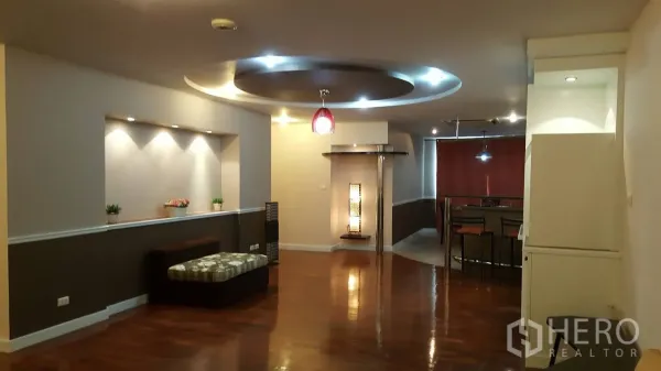 公寓 出租在Khlong Toei, Bangkok - 宽敞起居区，亮面木地板、嵌灯展示壁龛与圆形吊顶，通往用餐区