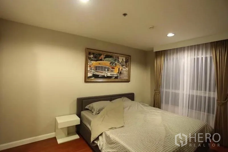 คอนโด ให้เช่าในHuai Khwang, Bangkok - ห้องนอนใหญ่เตียงควีน โต๊ะหัวเตียง ผ้าม่าน และกรอบภาพเหนือหัวเตียง