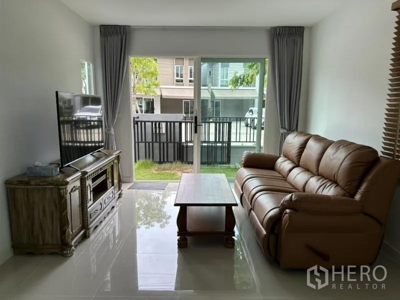 ทาวน์เฮาส์ ให้เช่าในBang Phli, Samut Prakan - ห้องนั่งเล่น โซฟาหนัง ทีวี และประตูเลื่อนออกสวนหน้าบ้าน
