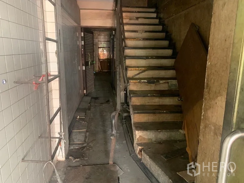 Shophouse for rent in Watthana, Bangkok - Narrow passage with wooden staircase and shuttered rear section.