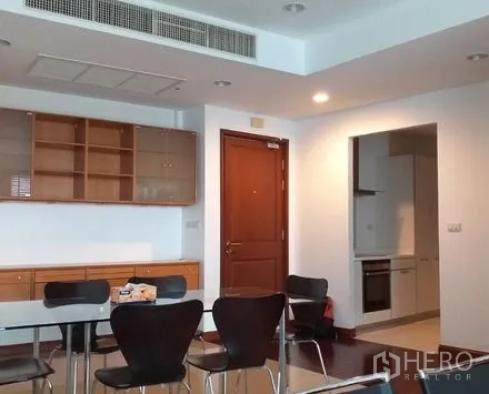 Condominium for rent in Pathum Wan, Bangkok - Dining area with built-in shelving, wooden door, and entry to a compact kitchen.