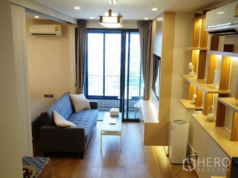 公寓 出租在Ratchathewi, Bangkok - 明亮客厅带沙发与置物架，落地窗通往城市景观阳台。