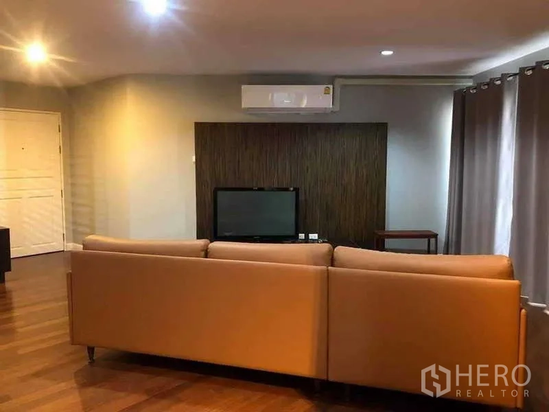 Condominium for sale in Yan Nawa, Bangkok - Lounge view showing TV wall behind a tan sectional sofa.