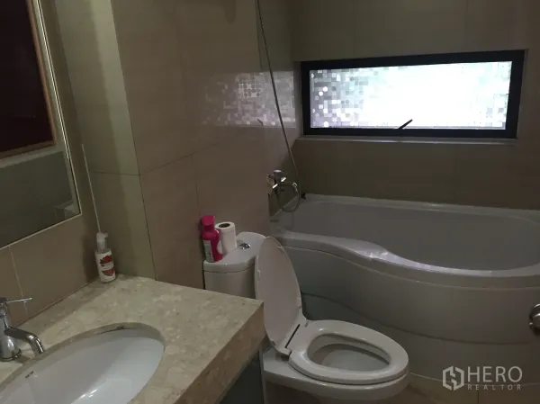 公寓 出租在Pathum Wan, Bangkok - 现代浴室，石材台面洗手盆、坐便器与弧形浴缸，配磨砂窗。