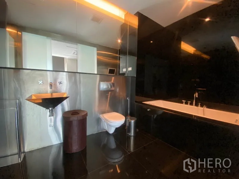 Condominium for rent in Sathon, Bangkok - Luxurious bathroom with deep soaking bathtub, black tile walls and a sleek metal sink.