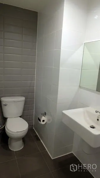Condominium for sale in Khlong Toei, Bangkok - Clean bathroom featuring white sink, toilet and gray textured tile accent wall.