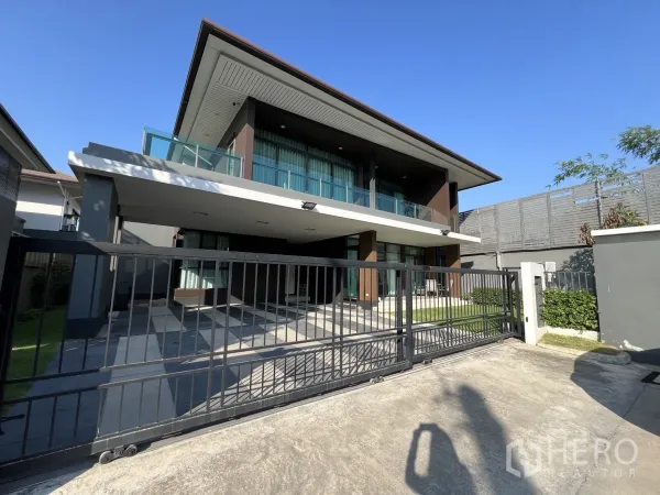 独立式住宅 出租或出售在Bang Kapi, Bangkok - 正门视角，滑动铁门与宽阔车道，晴空之下的两层住宅。
