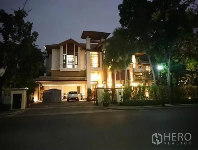 独立式住宅 出租在Khlong Toei, Bangkok - 黄昏时分点灯的两层独栋别墅外观，带大门车道与有顶车位，街景葱郁。