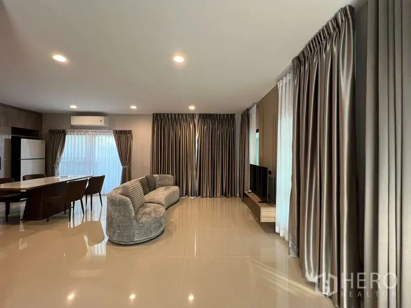 Detached House for rent in Bang Kapi, Bangkok - Open-plan living and dining area with curved sofa, TV and full-length curtains.