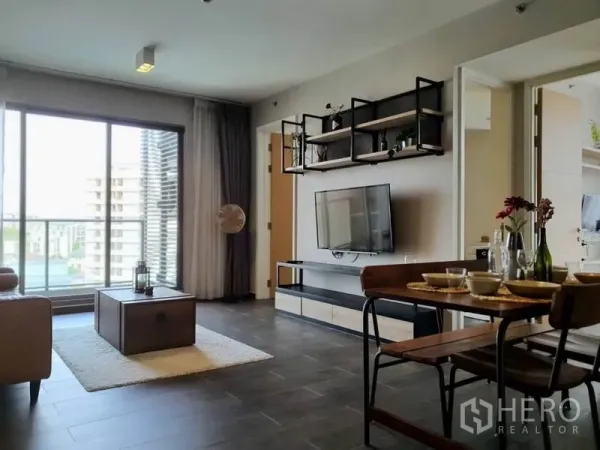 公寓 出租或出售在Watthana, Bangkok - 明亮客厅带落地窗与阳台景观，墙面挂装电视。