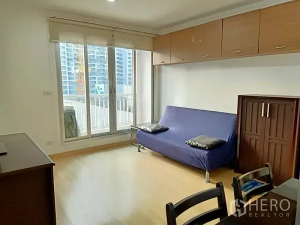Condominium for rent in Bang Rak, Bangkok - Bright living room with sliding glass doors to a balcony, wood floors and wall cabinets overlooking the city.