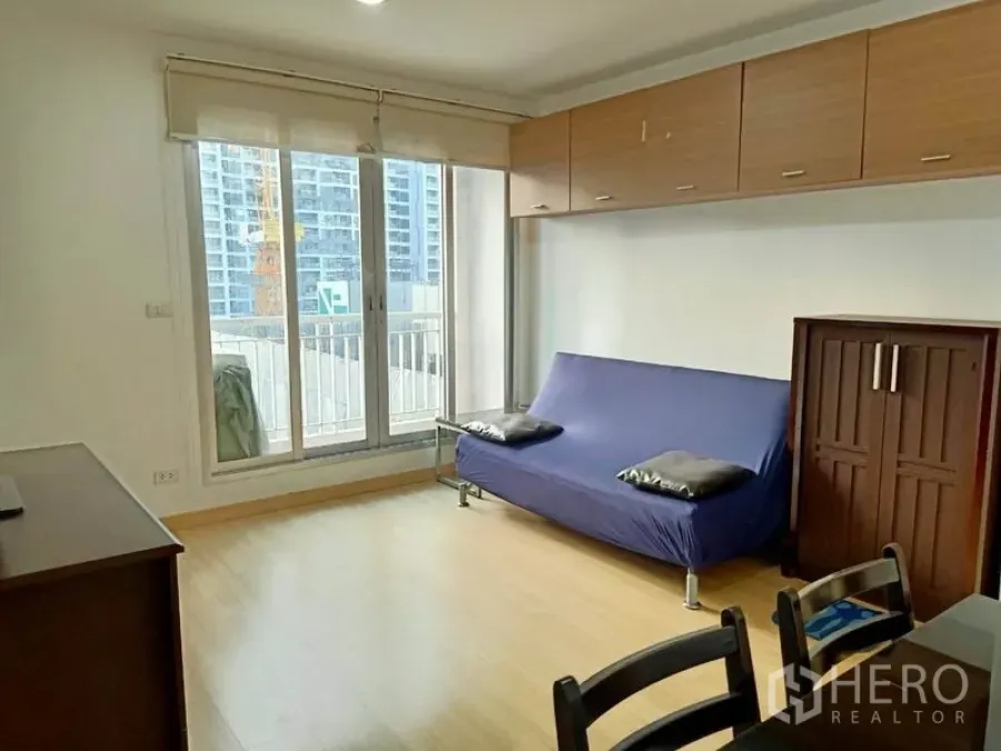 公寓 出租在Bang Rak, Bangkok - 明亮客厅，落地推拉门连通阳台，木地板与吊柜，可见城市景观。