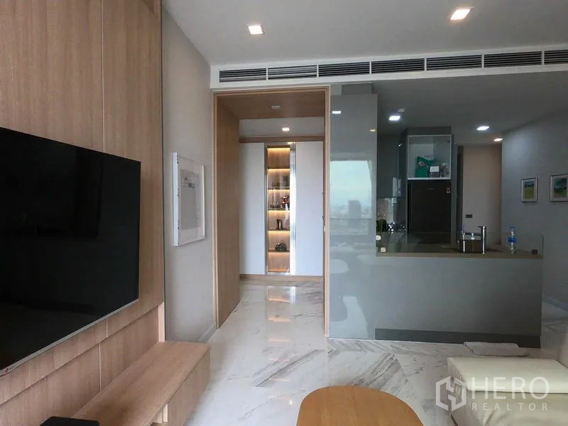 Condominium for rent or sale in Bang Rak, Bangkok - Open-plan living area with a gray kitchen, marble floors, and wall-mounted TV.