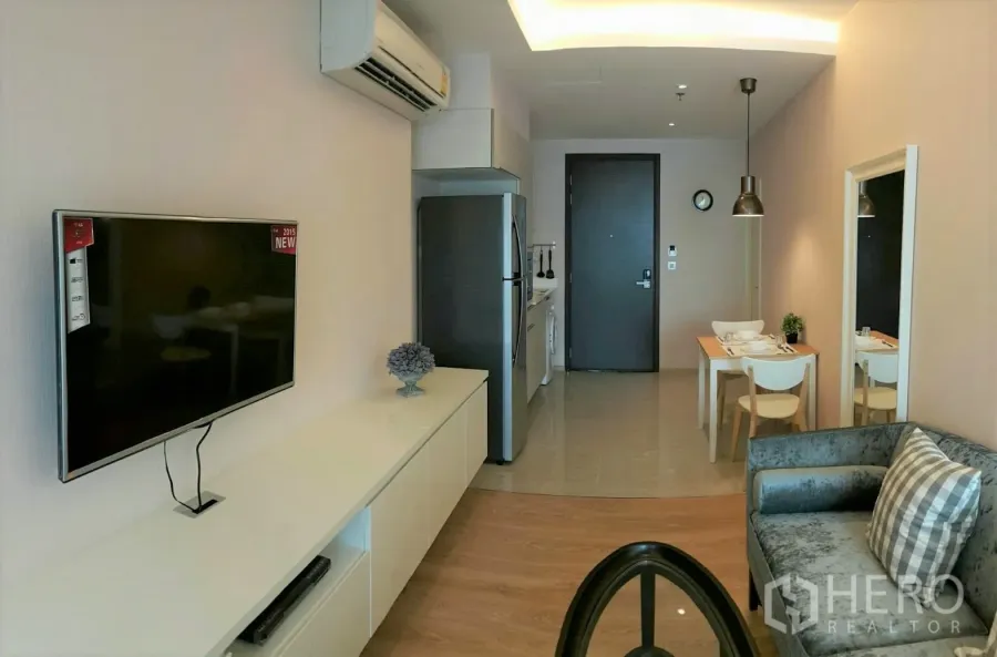公寓 出租在Watthana, Bangkok - 明亮客厅，设壁挂电视、空调、沙发和紧邻小厨房的用餐角。