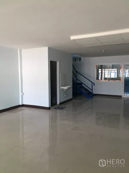 Warehouse for rent in Bueng Kum, Bangkok - Bright ground-floor office area with glossy tile flooring, a sink, and a blue staircase.