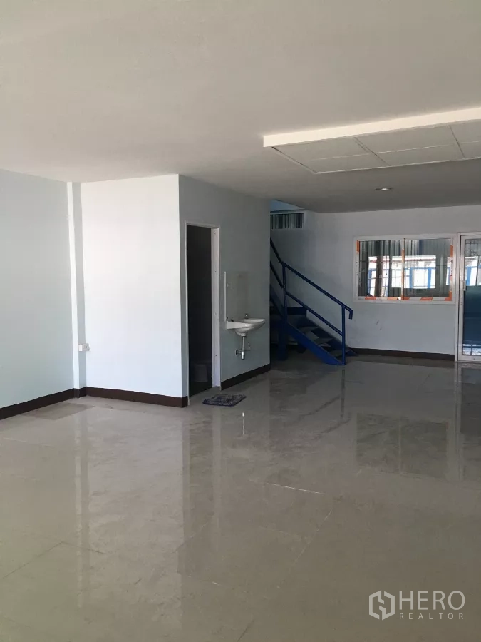 Warehouse for rent in Bueng Kum, Bangkok - Bright ground-floor office area with glossy tile flooring, a sink, and a blue staircase.