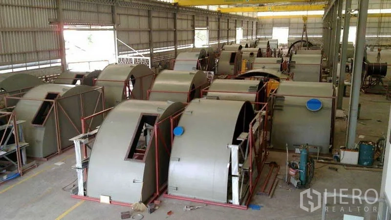 Factory for sale in Chachoengsao - Manufacturing area with large cylindrical metal casings arranged in frames beneath cranes.