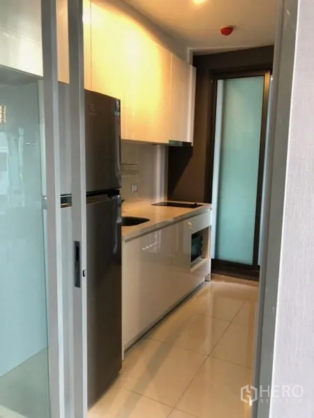 Condominium for rent in Khlong Toei, Bangkok - Compact galley kitchen with built-in cabinetry, cooktop, oven, and refrigerator.