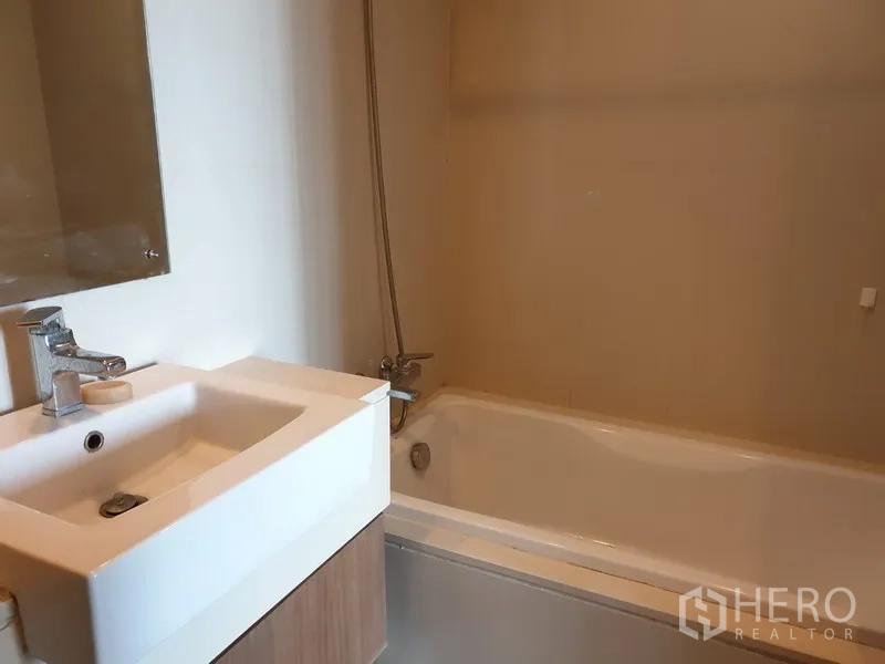 公寓 出租在Watthana, Bangkok - 浴室配白色洗手台、镜面与带手持花洒的浴缸。