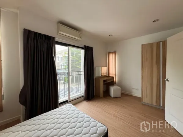 Townhouse for rent in Bang Kapi, Bangkok - Bright bedroom with balcony sliding door, desk and wardrobe, wood flooring.