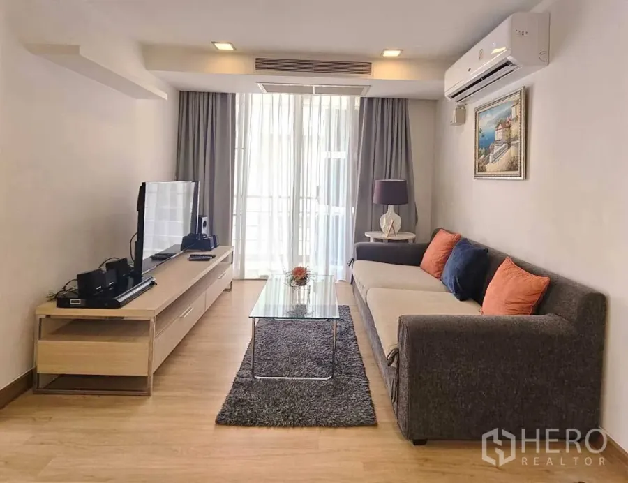 公寓 出租在Watthana, Bangkok - 明亮客厅，长沙发、电视柜、玻璃茶几与通向阳台的落地门。