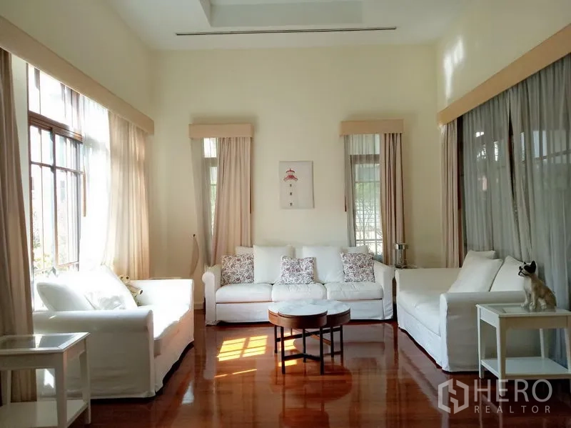 บ้าน ให้เช่าในWatthana, Bangkok - ห้องนั่งเล่นโปร่งเพดานสูง หน้าต่างบานใหญ่ โซฟาสีขาว ผ้าม่านโปร่ง และพื้นไม้เงางาม