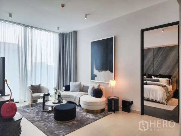 公寓 出租在Bang Rak, Bangkok - 明亮客厅，弧形沙发与抽象画作，连通卧室的门。