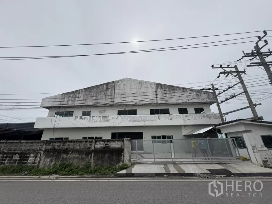 Factory for rent in Khlong Toei, Bangkok - Street-side view of a two-storey standalone factory with gated entrance and power lines.