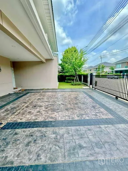 独立式住宅 出售在Lat Krabang, Bangkok - 有顶车库与铺砖车道，旁边是前院草地与大门。
