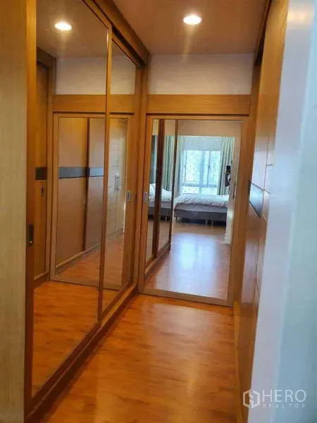 Detached House for rent in Saphan Sung, Bangkok - Hallway with mirrored built‑in wardrobes and warm wood flooring leading toward a bright bedroom.
