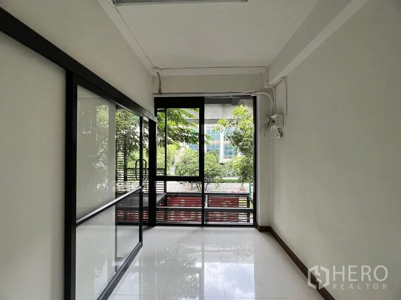 Shophouse for rent in Khlong Toei, Bangkok - Street-facing glass storefront with sliding doors and views of trees outside.