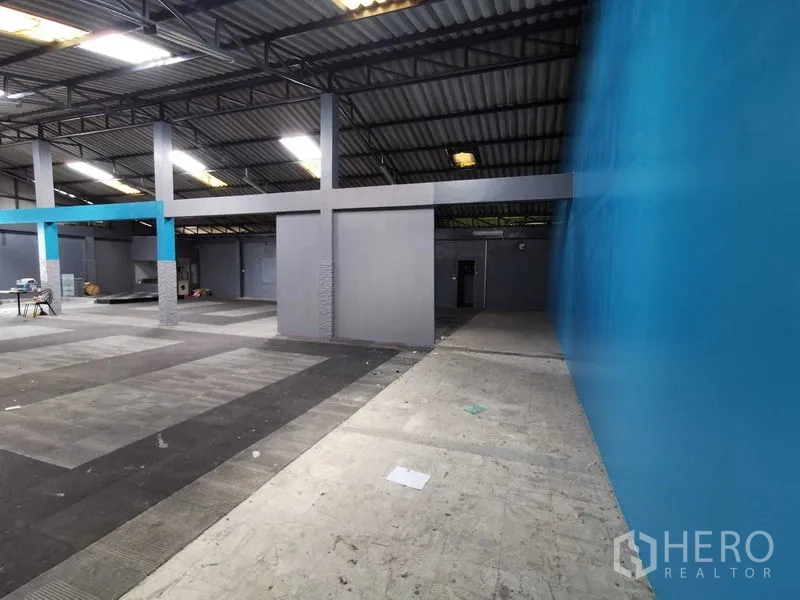 Warehouse for rent in Nonthaburi - Aisle beside a blue wall leading to open warehouse space and gray partition units.