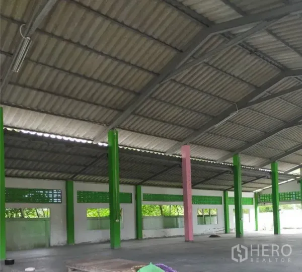 Factory for rent or sale in Samut Prakan - Spacious factory hall with high metal roof, green support columns, ventilation blocks and concrete floor.