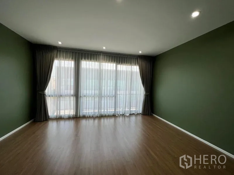 Townhouse for rent in Saphan Sung, Bangkok - Spacious empty room with green accent walls, wood flooring and wide windows with drapes.