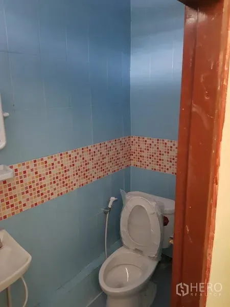 Retail Space for rent in Khlong Toei, Bangkok - Compact bathroom with blue wall tiles, mosaic accent band, toilet and handheld bidet sprayer.