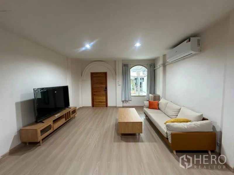 Townhouse for rent or sale in Phra Khanong, Bangkok - Spacious living room with arched feature window and neutral decor.