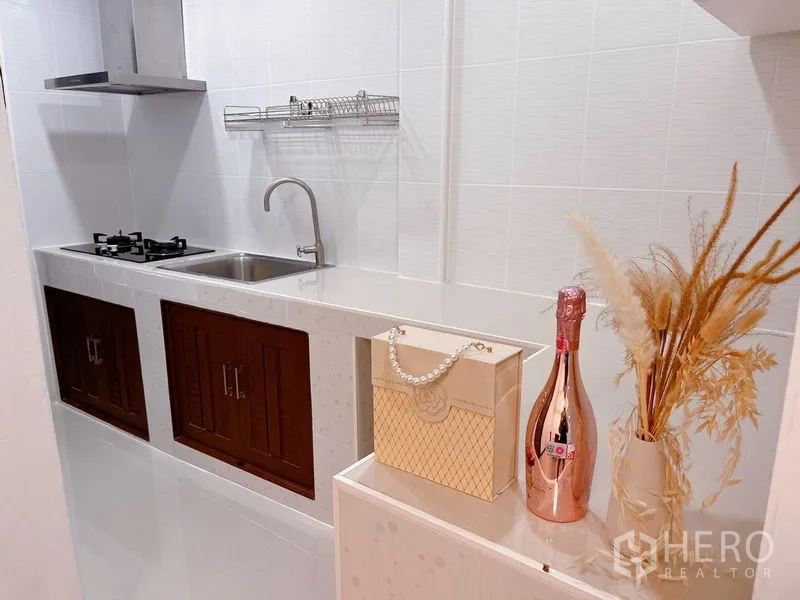 Townhouse for rent in Huai Khwang, Bangkok - Compact white kitchen with gas hob, sink, backsplash and decorative accents.