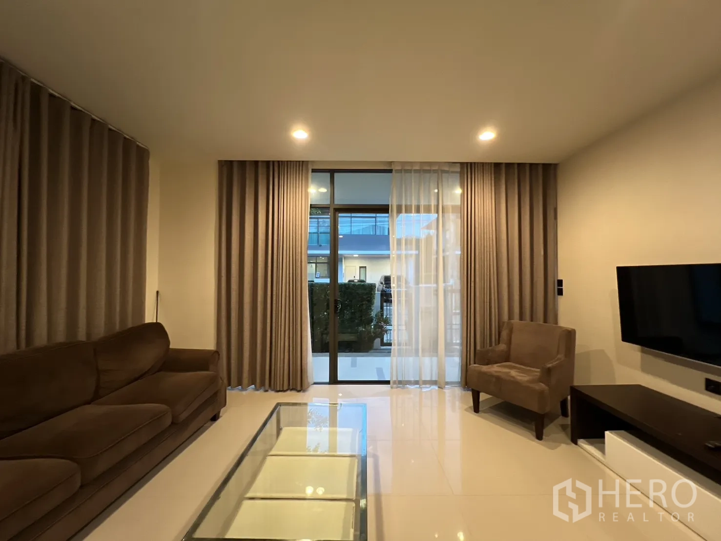 Detached House for rent or sale in Bang Kapi, Bangkok - Lounge with floor-to-ceiling glass doors and TV wall unit.