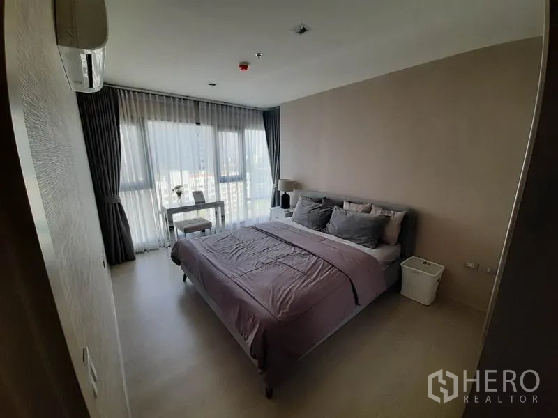 Condominium for rent or sale in Khlong Toei, Bangkok - Bright bedroom with large windows, city view, bed and a small desk.