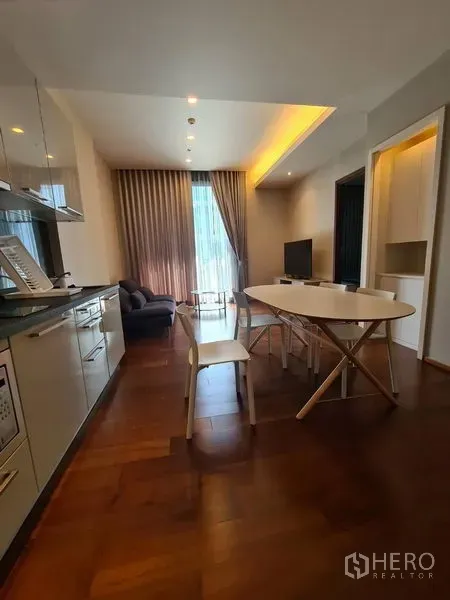 Condominium for rent in Watthana, Bangkok - Living area with sofa, TV console, dining table and recessed ceiling lights beside a tall window.