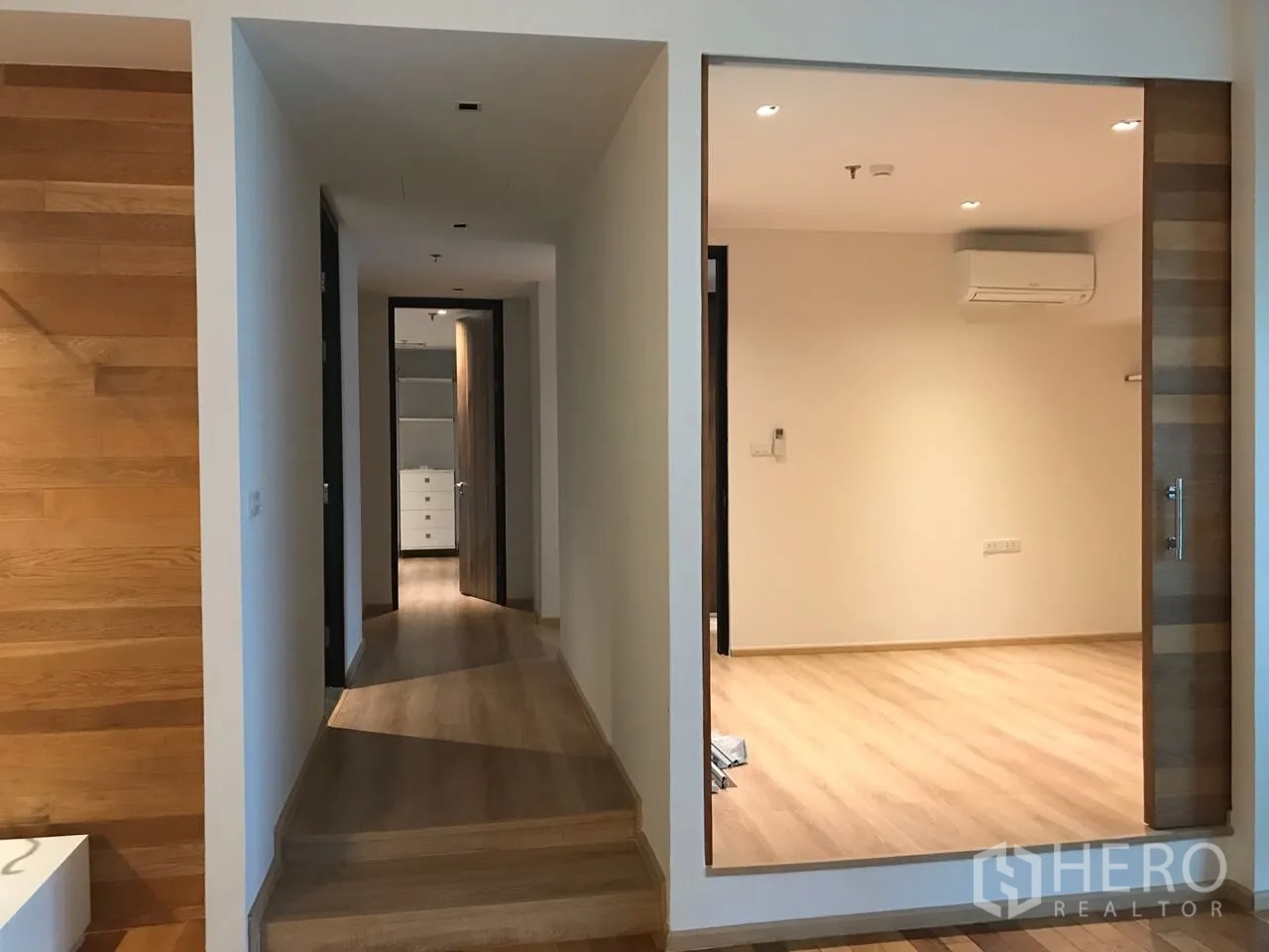 Condominium for rent in Khlong Toei, Bangkok - Corridor with a small step, adjoining glass-walled room and continuous wood floors.