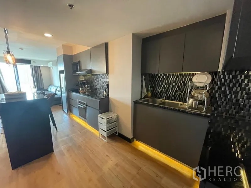 Condominium for sale in Chatuchak, Bangkok - Dual-counter kitchen with stainless sink, cooktop and under-cabinet lighting along a wood floor.
