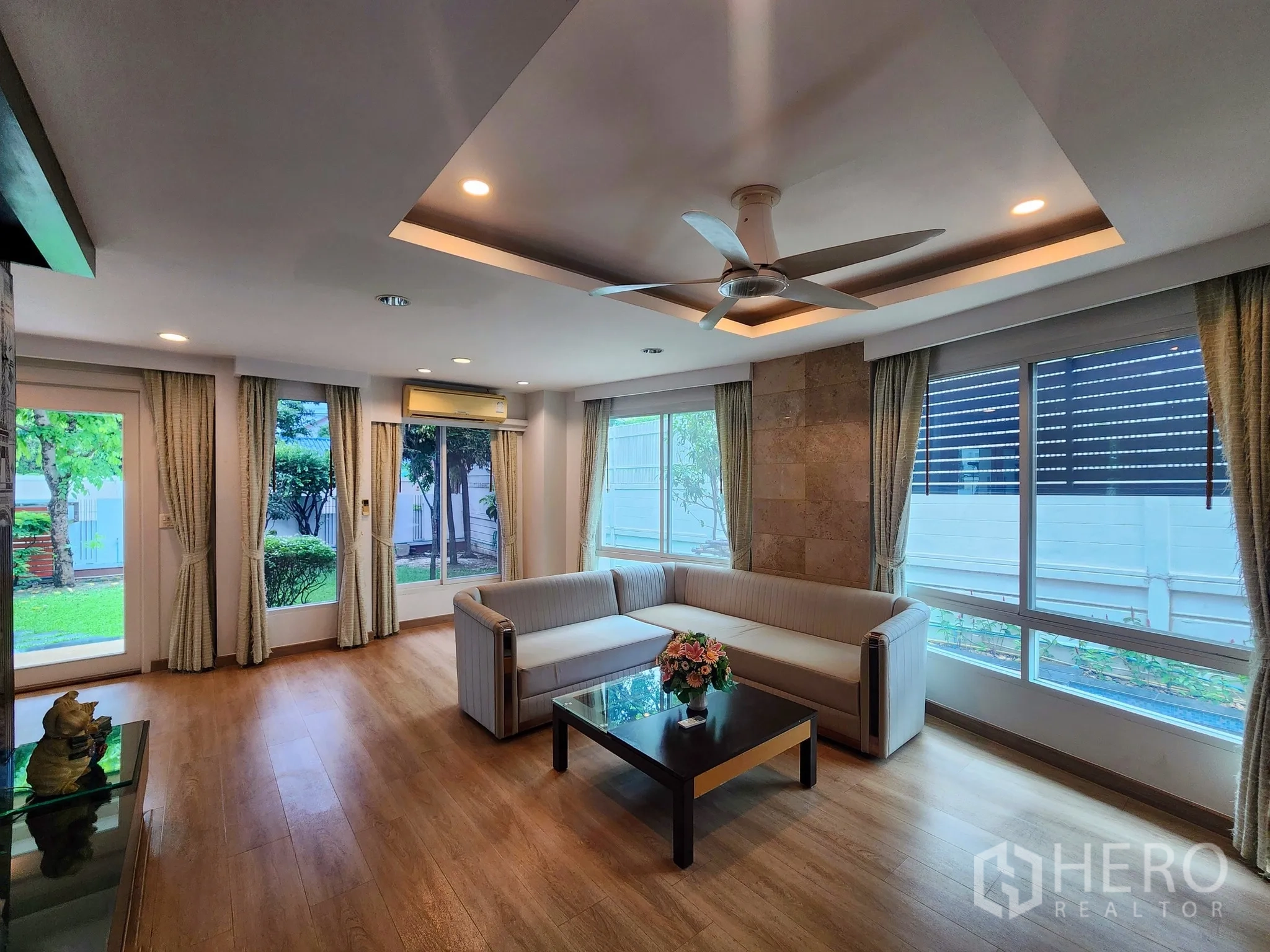 Detached House for rent in Bang Kapi, Bangkok - Living room with L-shaped sofa, ceiling fan, wood floors and garden views.