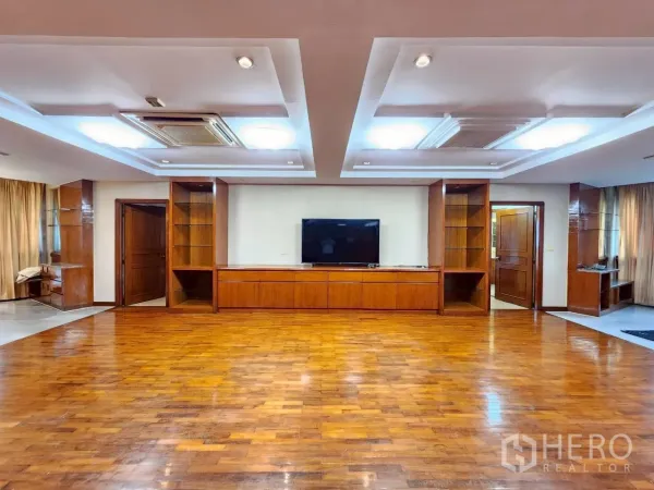 Condominium for rent in Khlong Toei, Bangkok - Large living space with coffered ceiling, TV and shelving framed by warm wood wall panels.