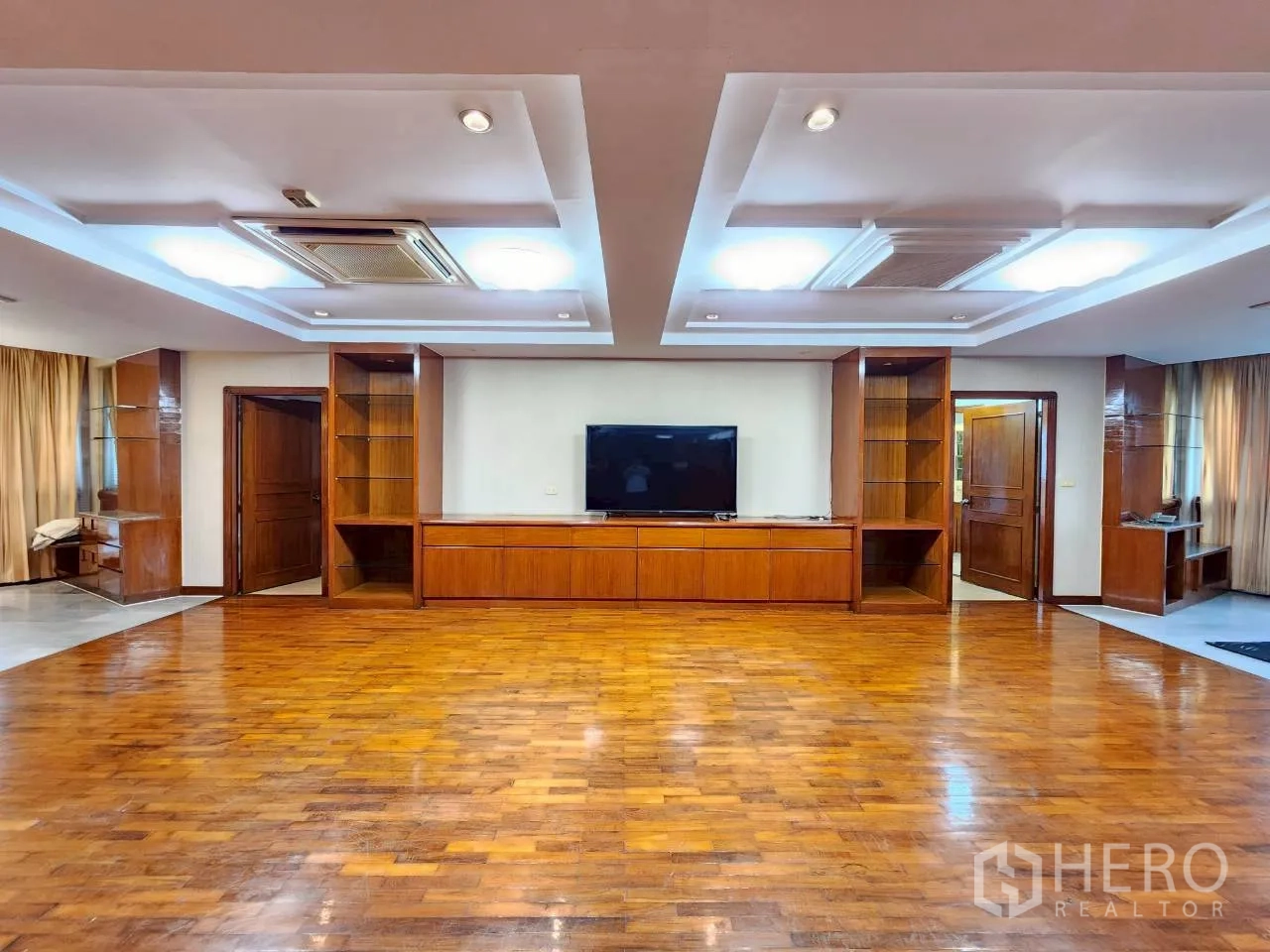 Condominium for rent in Khlong Toei, Bangkok - Large living space with coffered ceiling, TV and shelving framed by warm wood wall panels.