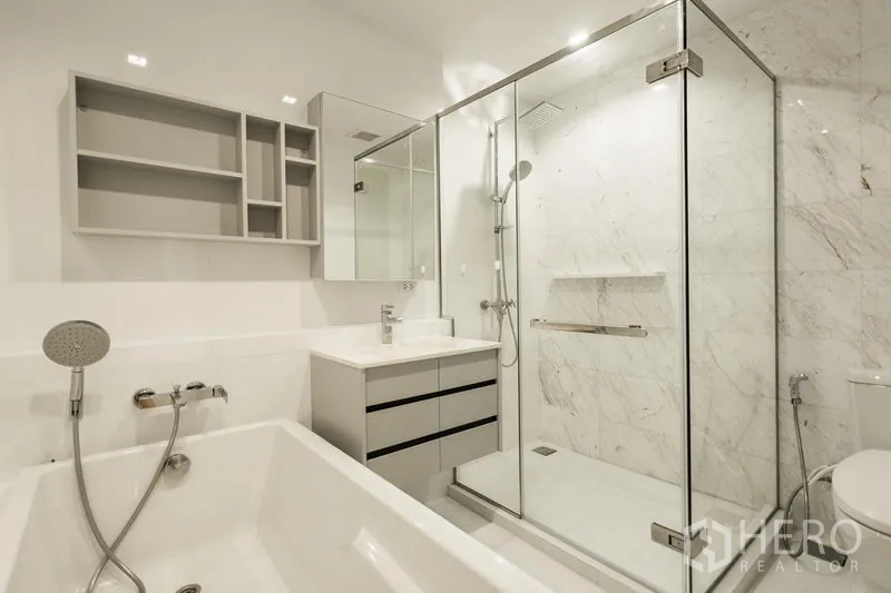 Condominium for rent in Watthana, Bangkok - White bathroom with soaking tub, glass‑enclosed rain shower, vanity and toilet.