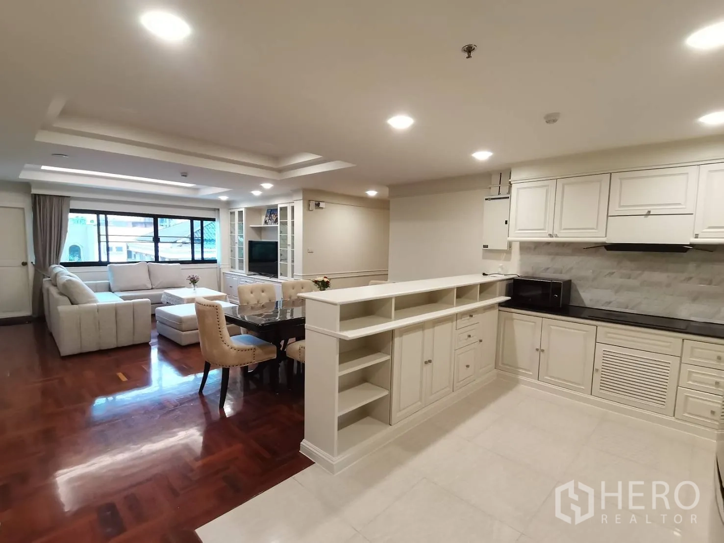 公寓 for rent in Watthana, Bangkok - 开放式客厅，L形沙发、餐桌与白色厨房，嵌灯与木地板。