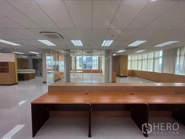 Office Space for rent in Suan Luang, Bangkok - Open-plan office with glass-partitioned meeting room, long bench desks, grid lights, and wrap-around windows.