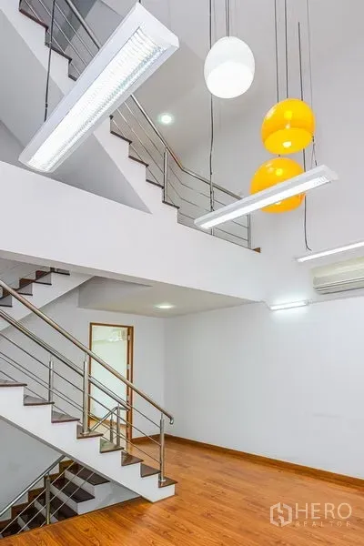 Townhouse for rent in Watthana, Bangkok - Open stair hall with warm wood floors, stainless-steel railings and contemporary pendant lights.