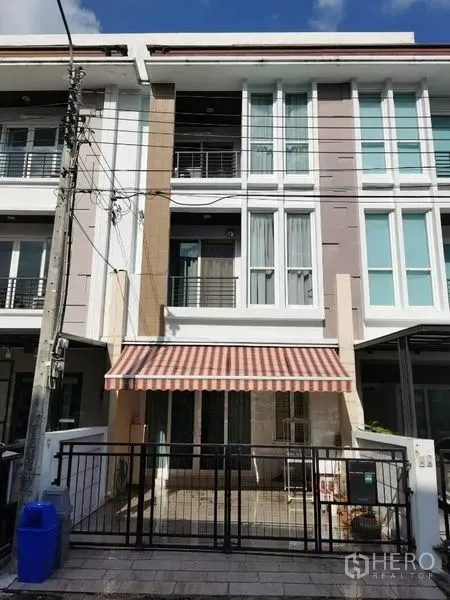 ทาวน์เฮาส์ ให้เช่าในWang Thonglang, Bangkok - ด้านหน้าทาวน์เฮ้าส์ 3 ชั้น มีกำแพงรั้วที่จอดรถและกันสาดลายทางในย่านวังทองหลาง